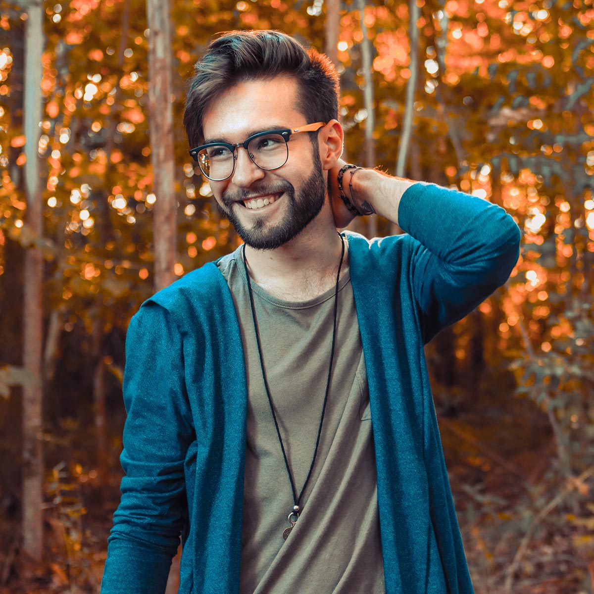 Man holding his neck showing off his new haircut in the forest.